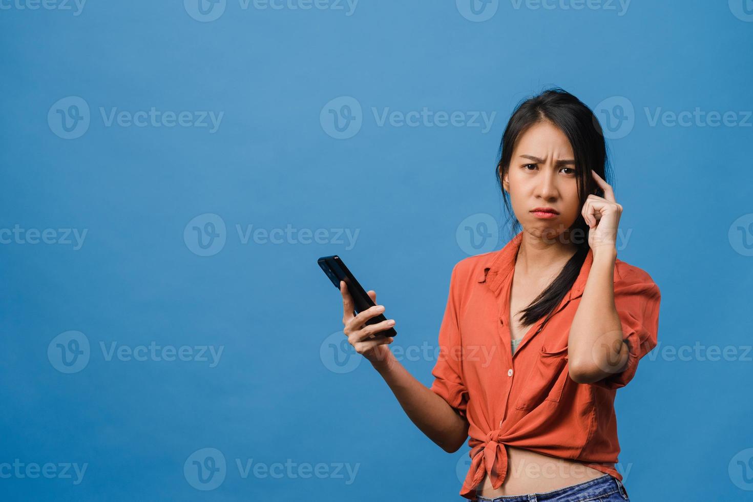 pensando di sognare una giovane donna asiatica che usa il telefono con un'espressione positiva, vestita con abiti casual, sentendo felicità e stando isolata su sfondo blu. felice adorabile donna felice esulta successo. foto