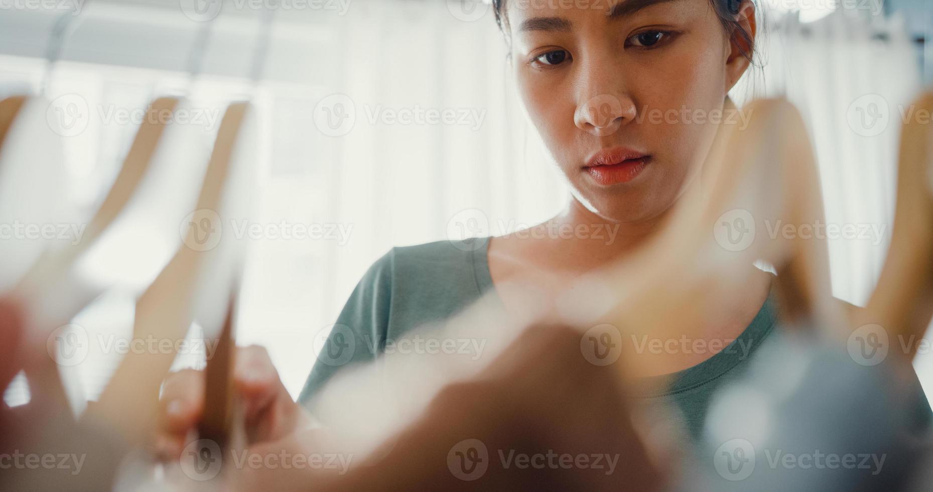 bella giovane signora asiatica attraente che sceglie i suoi vestiti di vestito di moda nell'armadio soggiorno a casa o in negozio. ragazza pensa a cosa indossare camicia casual. guardaroba di casa o spogliatoio del negozio di abbigliamento. foto