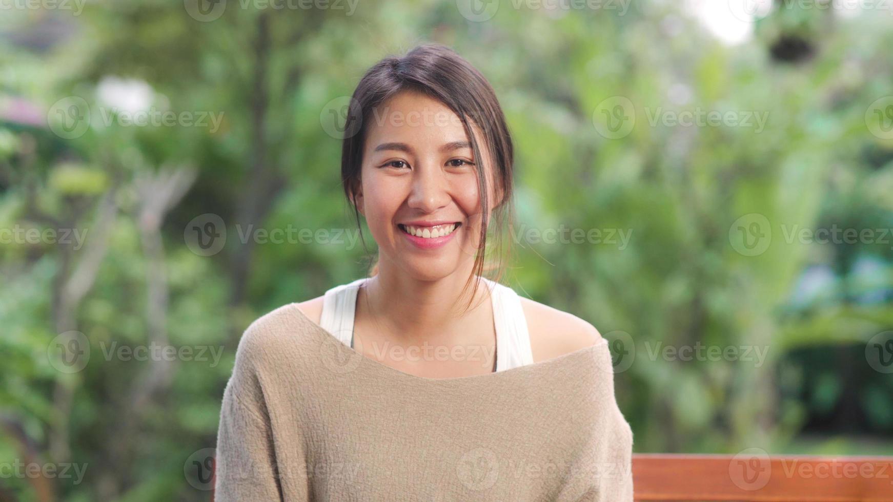 donna asiatica che si sente felice sorridente e guarda la telecamera mentre si rilassa sul tavolo in giardino a casa al mattino. le donne di stile di vita si rilassano a casa concetto. foto