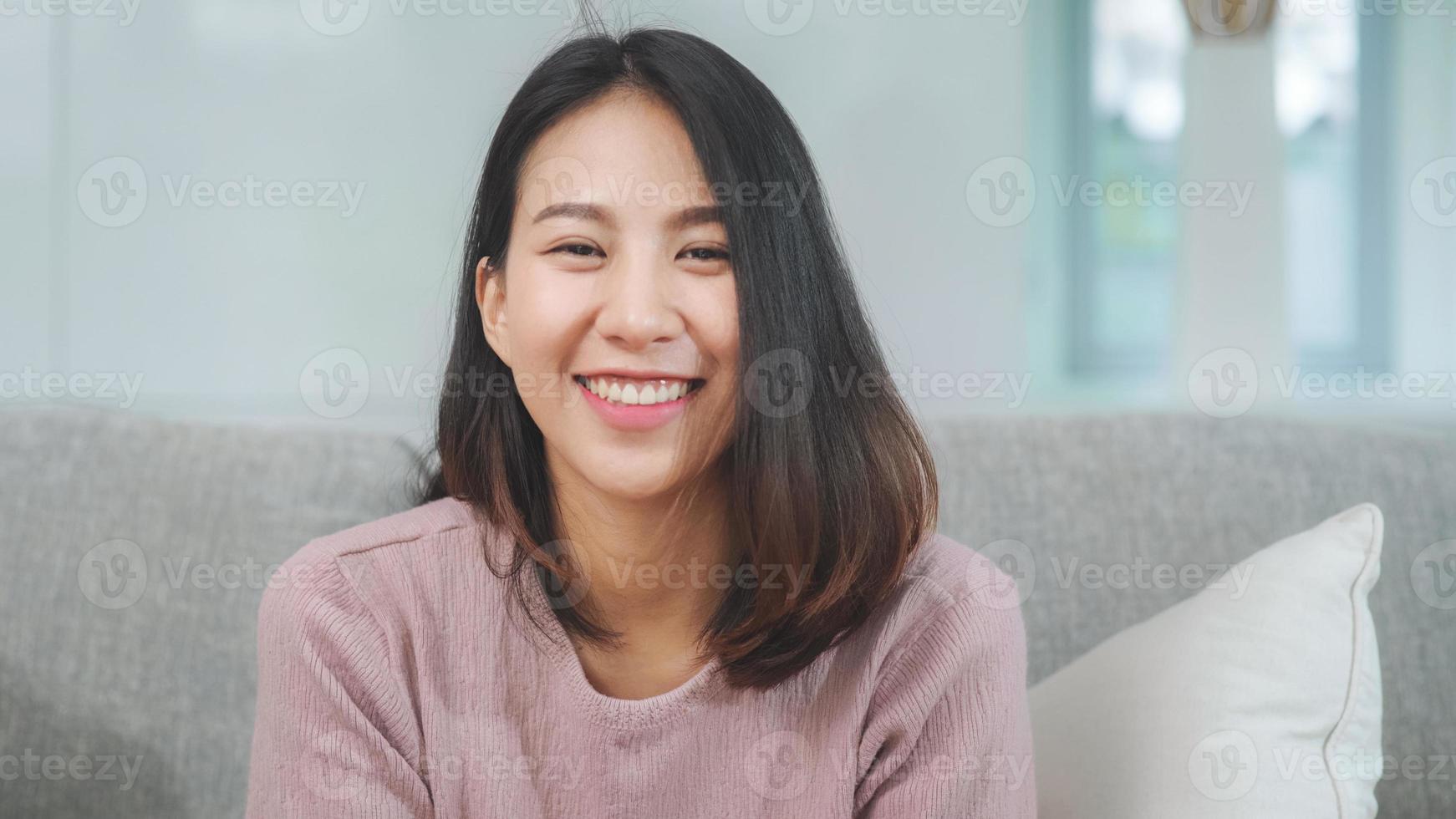 adolescente donna asiatica sentirsi felice sorridente e guardando la telecamera mentre si rilassa nel soggiorno di casa. stile di vita bella giovane donna asiatica che utilizza il concetto di tempo di relax a casa. foto