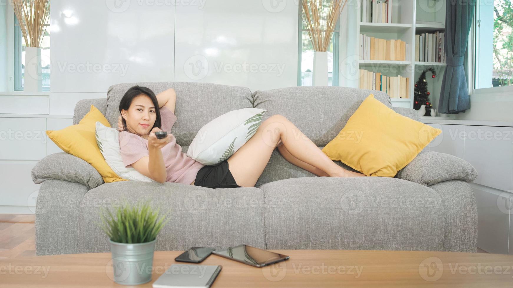 giovane donna adolescente asiatica che guarda la tv a casa, donna che si sente felice sdraiata sul divano in soggiorno. la donna di stile di vita si rilassa nel concetto di mattina a casa. foto