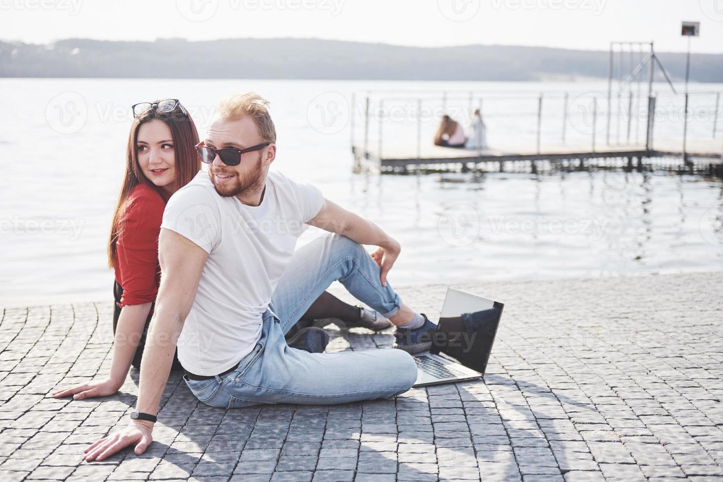 due studenti, ragazzo e ragazza, sono seduti all'aperto e si godono un laptop, studiando all'aperto in una giornata di sole foto