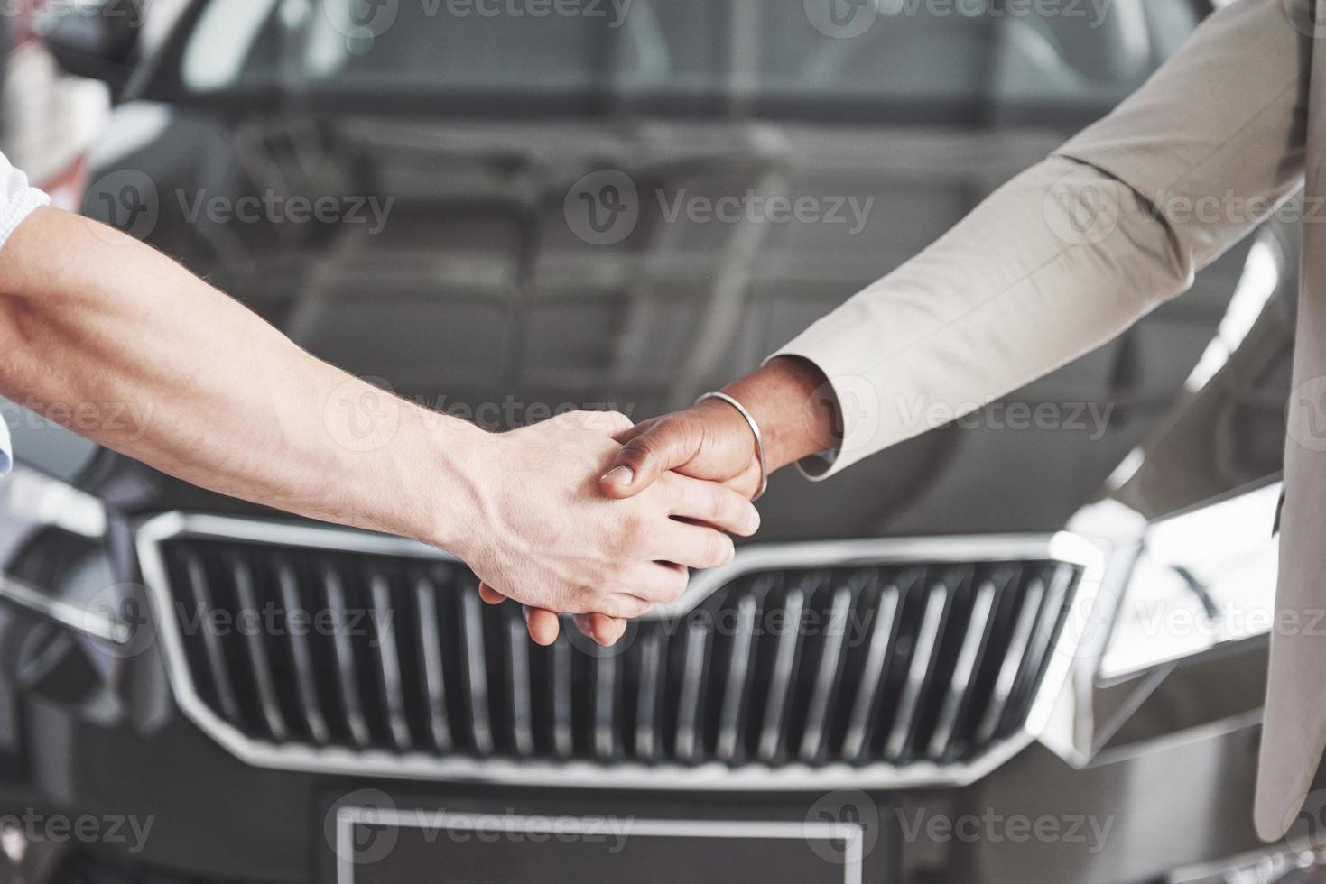 vista ravvicinata del concessionario e del nuovo proprietario che si stringono la mano nel salone di auto foto