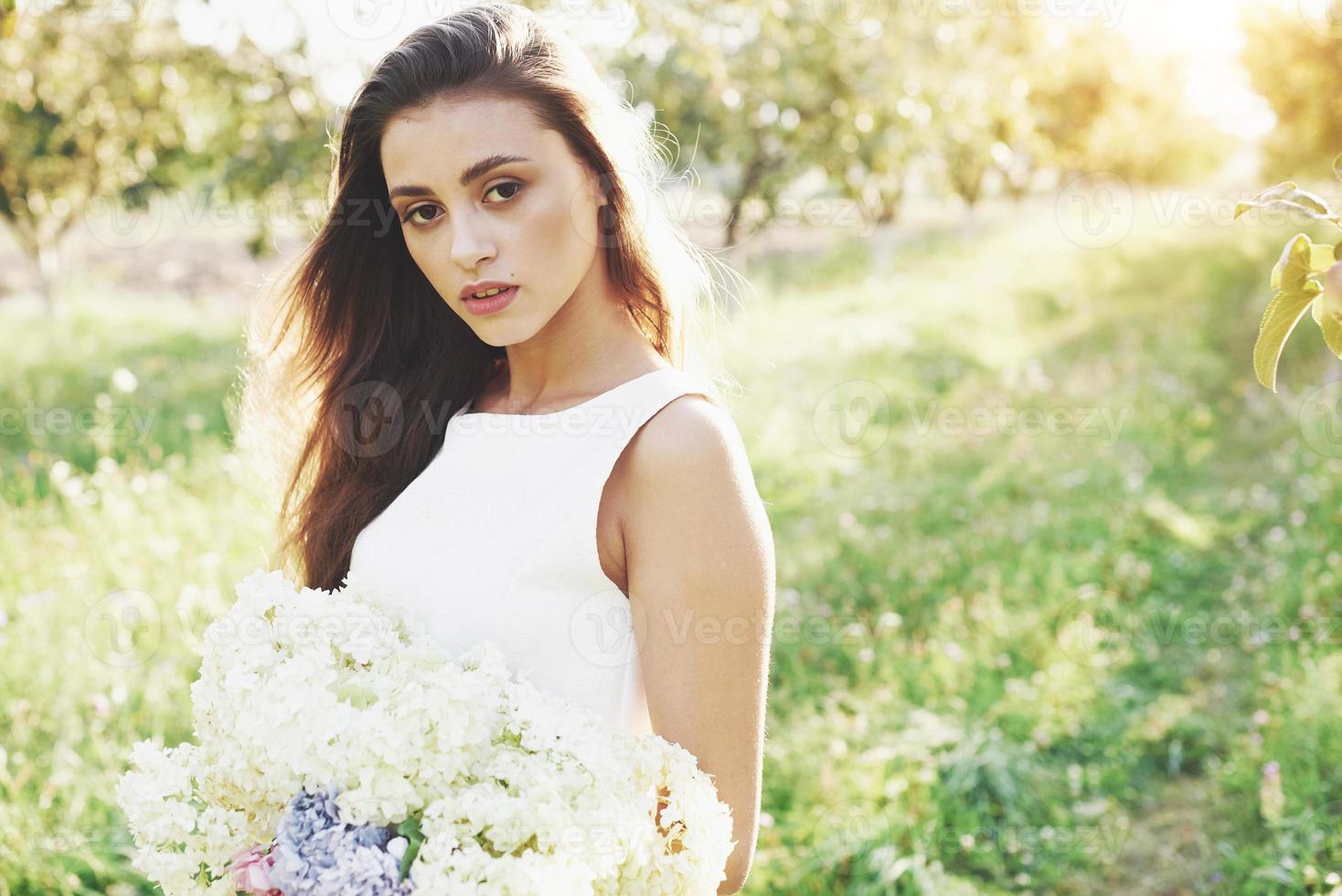 una bella ragazza con un vestito bianco chiaro e un mazzo di fiori estivi depone una bella giornata in giardino foto