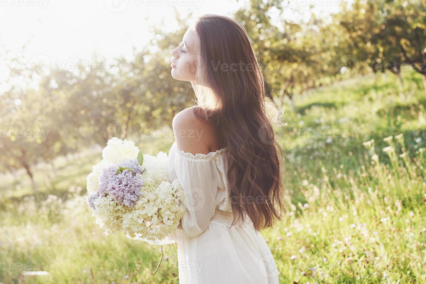 una bella ragazza con un vestito bianco chiaro e un mazzo di fiori estivi depone una bella giornata in giardino foto