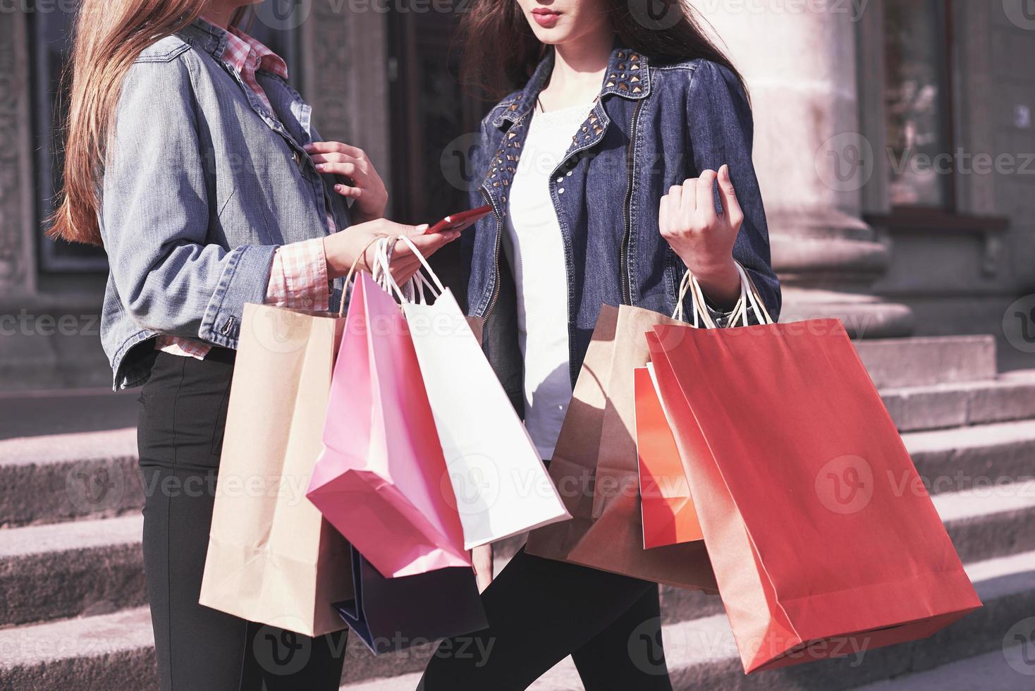 due giovani donne che trasportano borse della spesa mentre camminano per strada dopo aver visitato i negozi foto