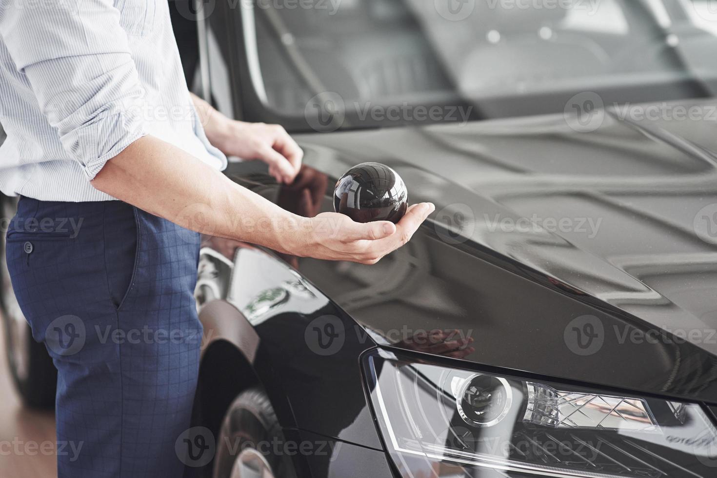 bel giovane consulente al salone di auto in piedi vicino all'auto. foto