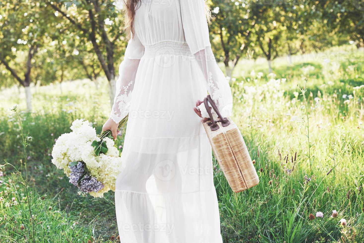 una bella ragazza con un vestito bianco chiaro e un mazzo di fiori estivi depone una bella giornata in giardino foto