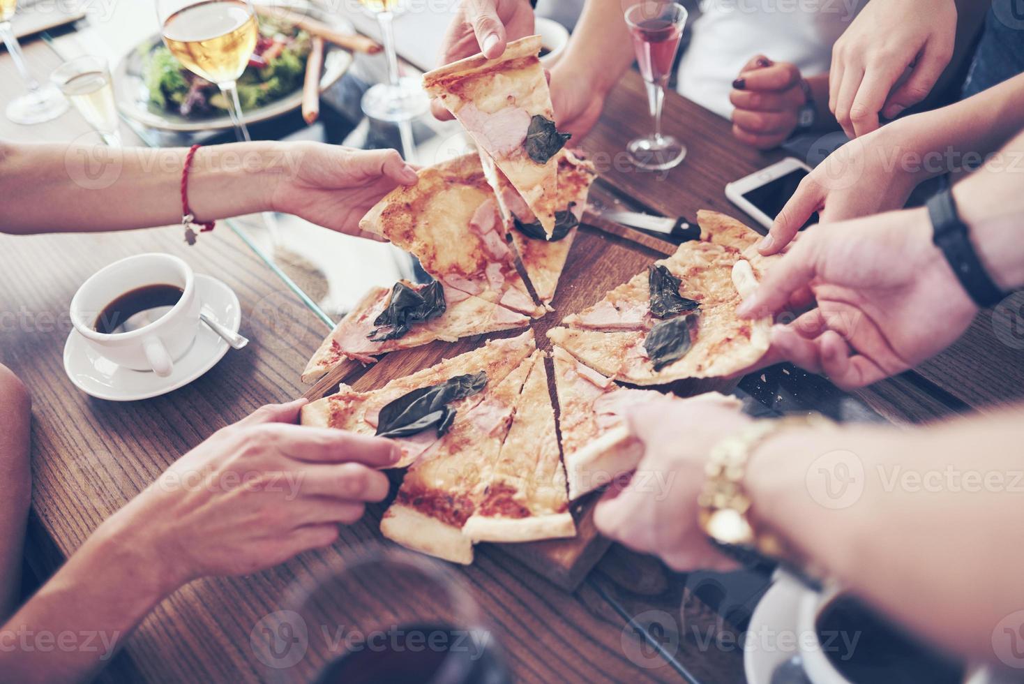 ora di cena. primo piano di gustosa pizza sul tavolo, con tante mani che prendono un pezzo foto