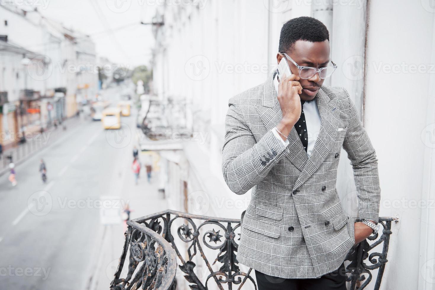 giovane africano in abbigliamento formale che parla al telefono cellulare e sorride mentre sta in piedi all'aperto foto