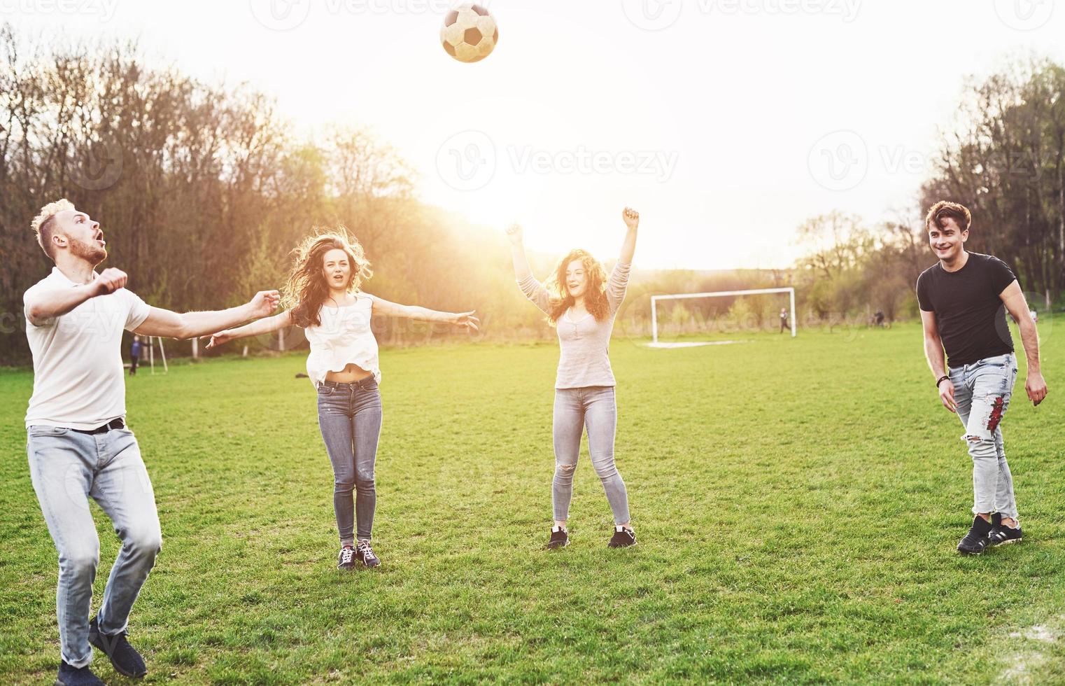 un gruppo di amici in abbigliamento casual gioca a calcio all'aria aperta. le persone si divertono e si divertono. riposo attivo e tramonto panoramico. foto