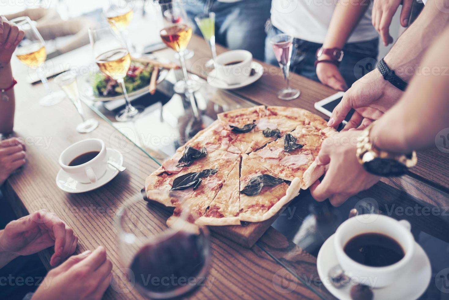 ora di cena. primo piano di gustosa pizza sul tavolo, con tante mani che prendono un pezzo foto