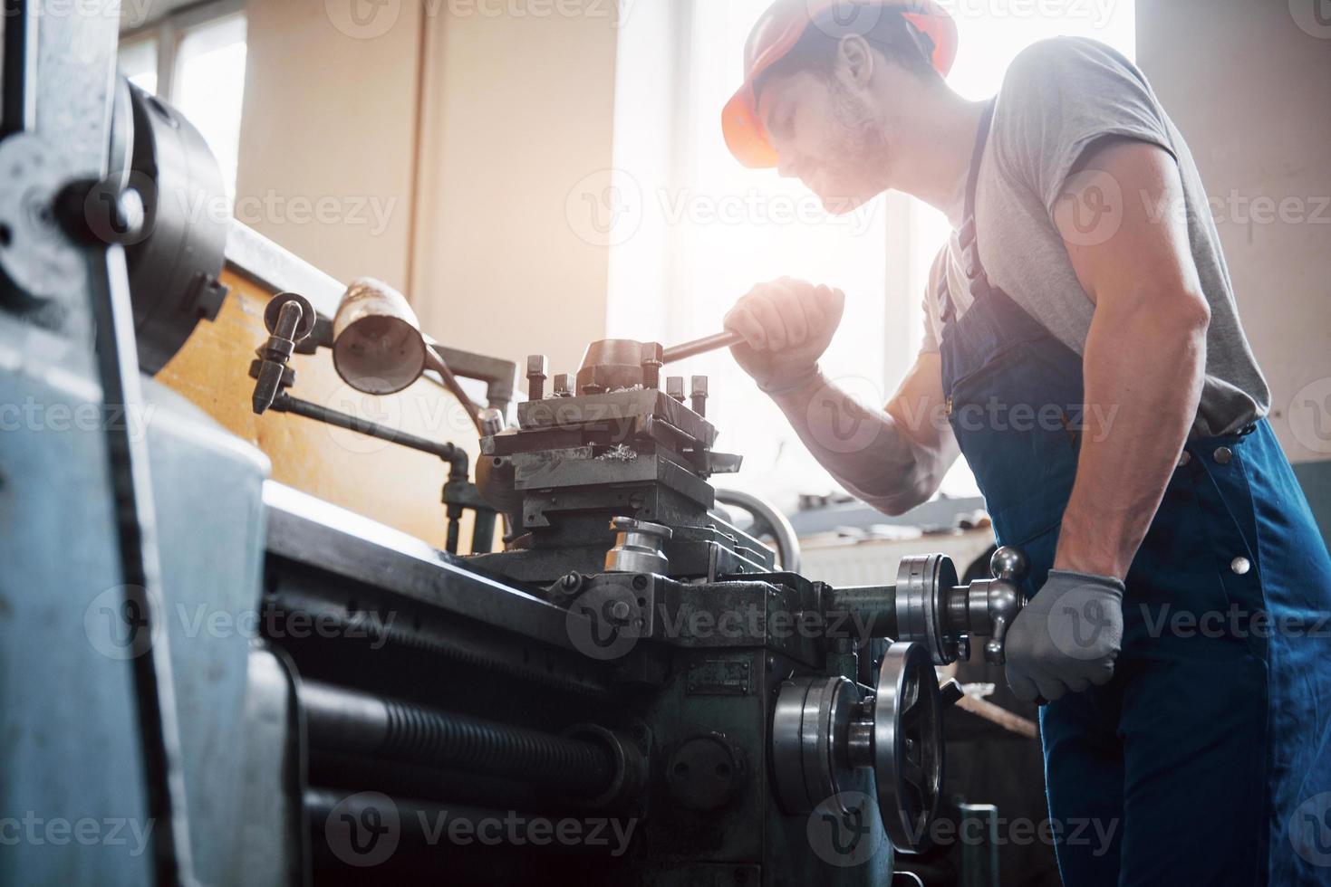 ritratto di un giovane lavoratore con un elmetto in un grande impianto di lavorazione dei metalli. l'ingegnere serve le macchine e produce parti per apparecchiature a gas foto