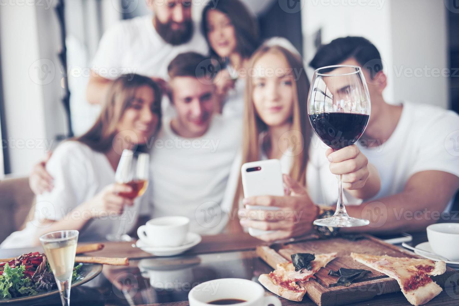 un gruppo di persone fa una foto selfie in un bar. i migliori amici si sono riuniti a tavola mangiando pizza e cantando vari drink