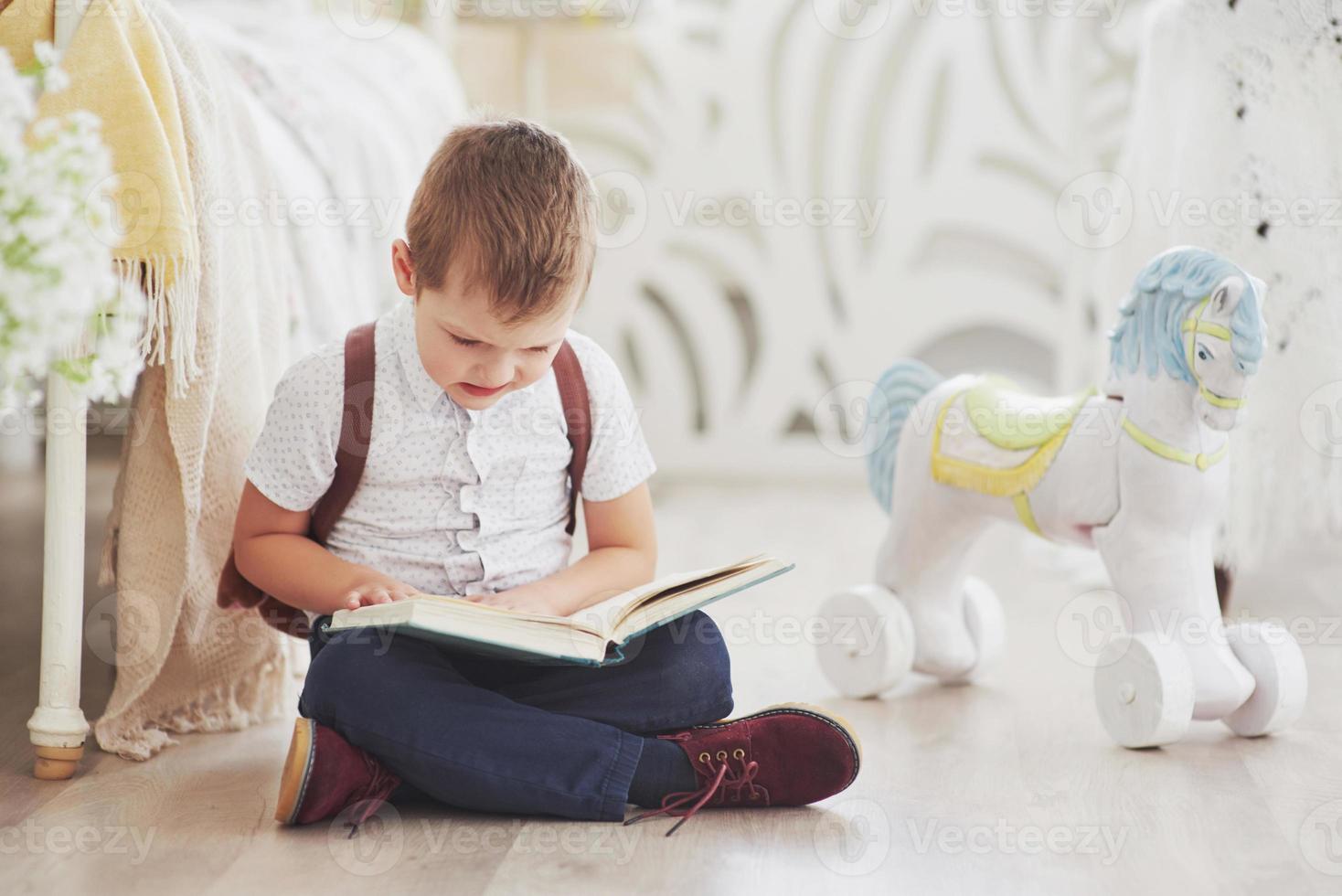 il ragazzino carino sta andando a scuola per la prima volta. bambino con borsa di scuola e libro. il bambino fa una valigetta, la stanza dei bambini su uno sfondo. di nuovo a scuola foto