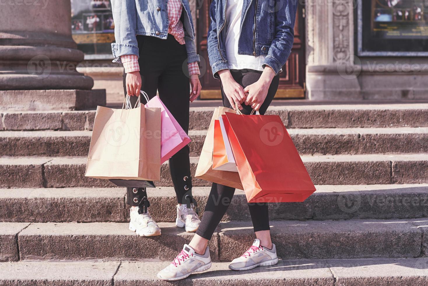 due giovani donne che trasportano le borse della spesa mentre camminano sulle scale dopo aver visitato i negozi foto