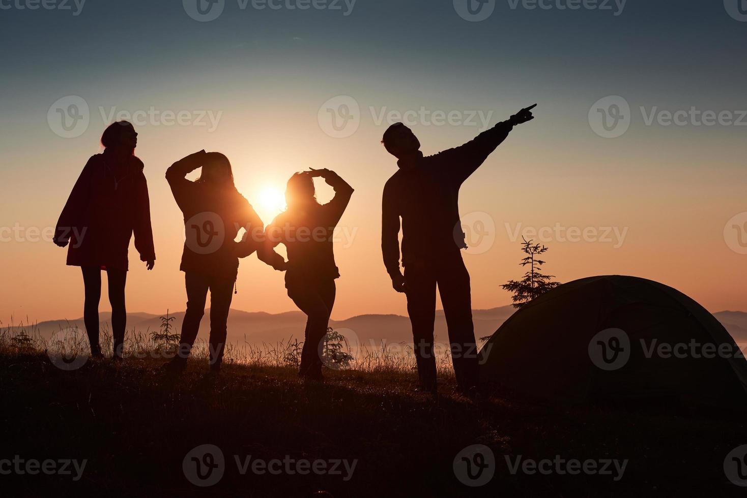 una silhouette di persone del gruppo si diverte in cima alla montagna vicino alla tenda durante il tramonto foto