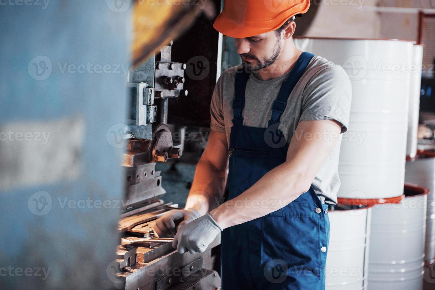 ritratto di un giovane lavoratore con un elmetto in un grande impianto di lavorazione dei metalli. l'ingegnere serve le macchine e produce parti per apparecchiature a gas foto