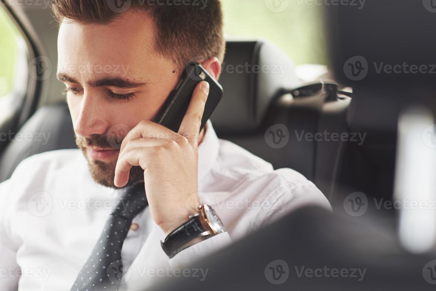 un uomo d'affari che invia un messaggio a uno smartphone e si avvicina al sedile posteriore dell'auto. foto