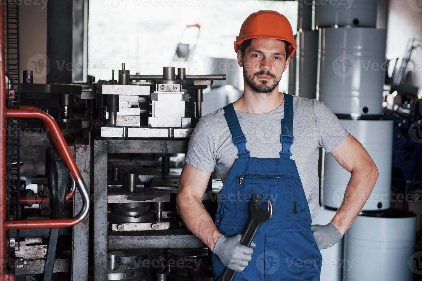 ritratto di un giovane lavoratore con un elmetto in un grande impianto di lavorazione dei metalli. l'ingegnere serve le macchine e produce parti per apparecchiature a gas foto