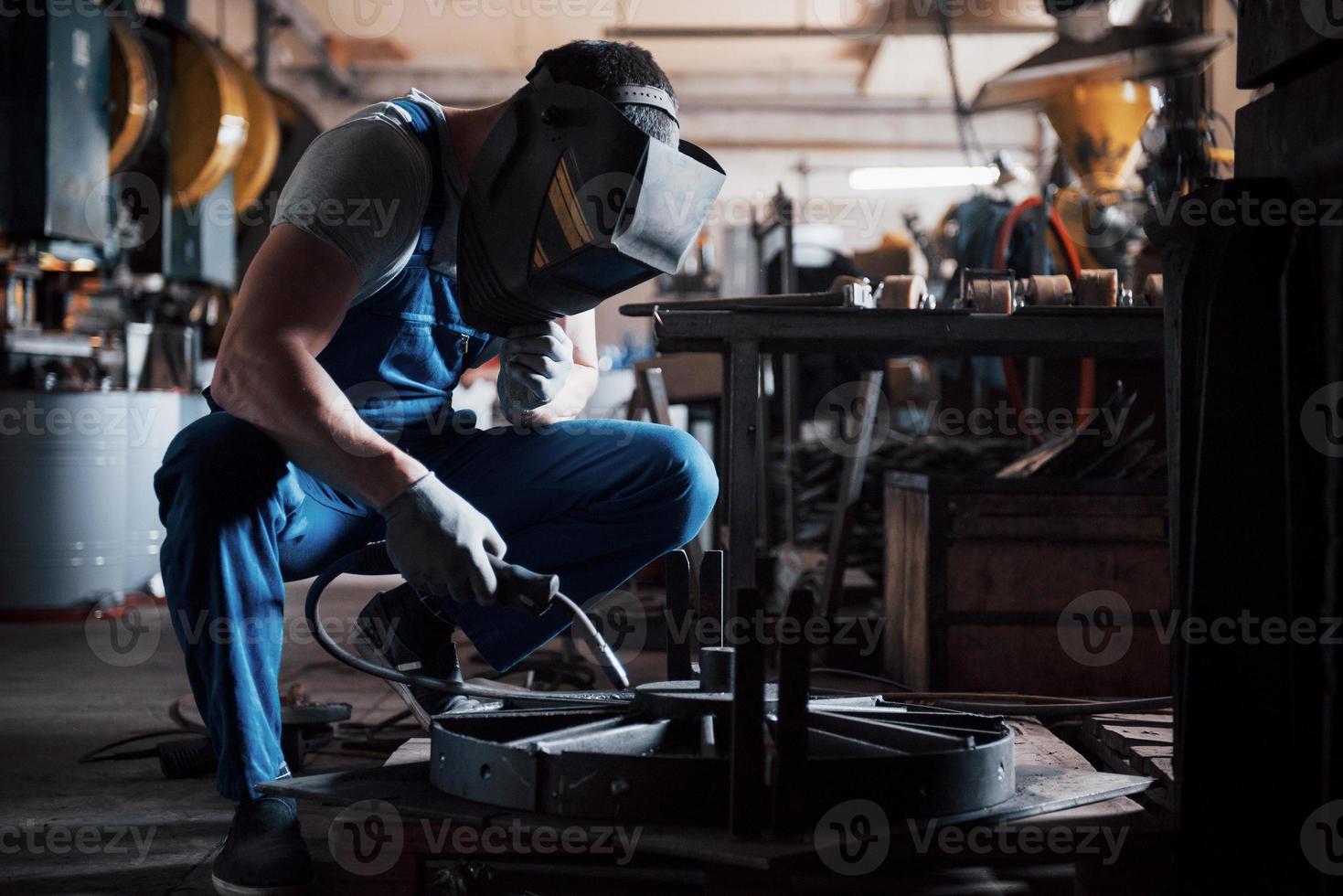 ritratto di un giovane lavoratore in un grande impianto di lavorazione dei metalli. l'ingegnere saldatore lavora con una maschera protettiva foto