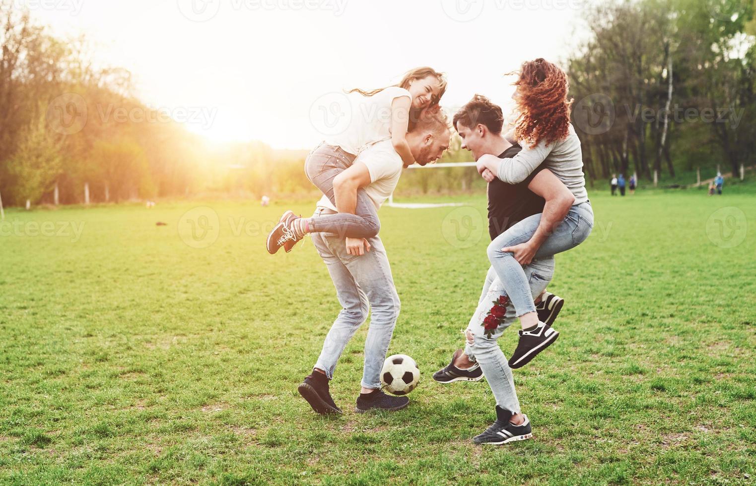 un gruppo di amici in abbigliamento casual gioca a calcio all'aria aperta. le persone si divertono e si divertono. riposo attivo e tramonto panoramico. foto