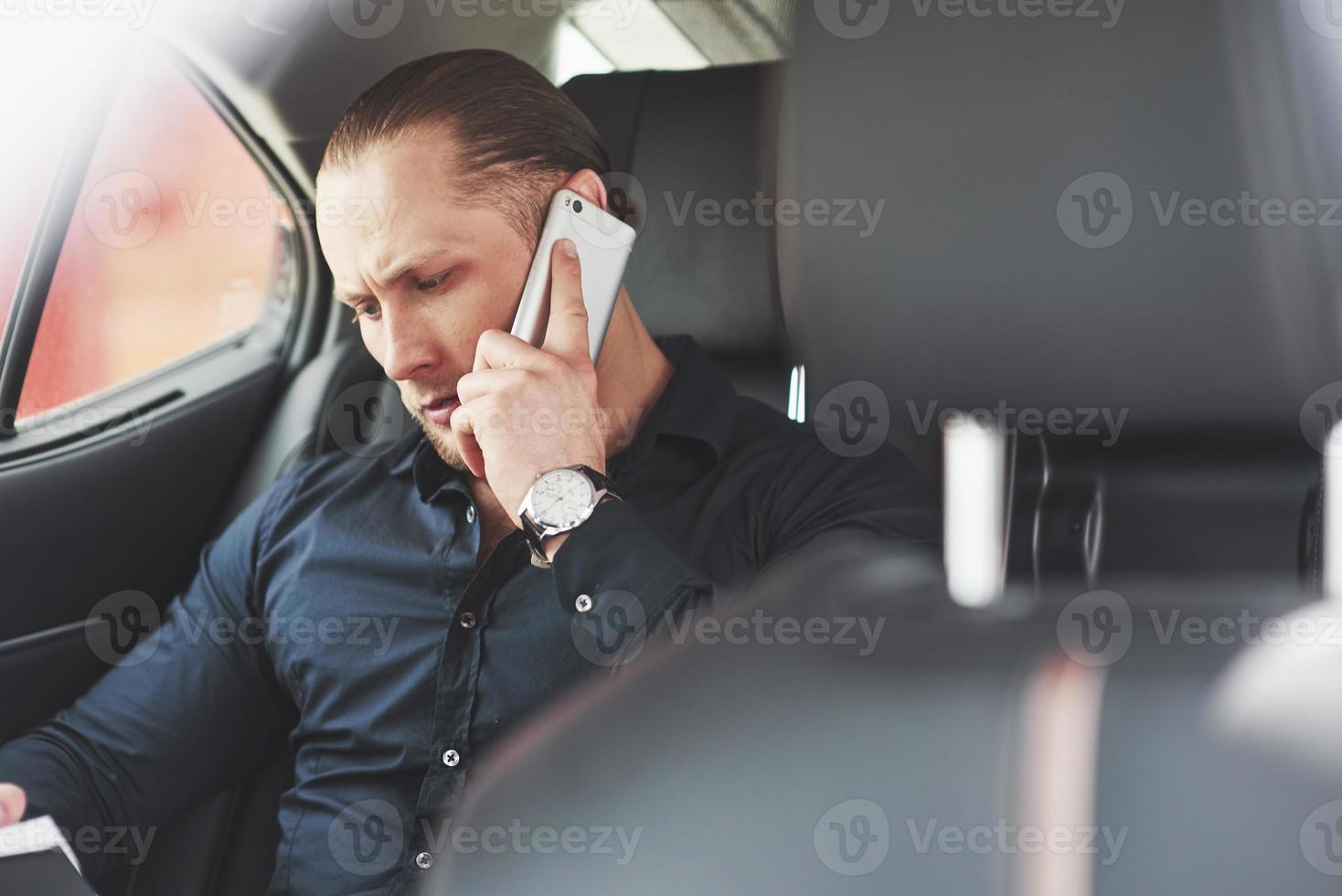 un uomo d'affari che invia un messaggio a uno smartphone e si avvicina al sedile posteriore dell'auto. foto