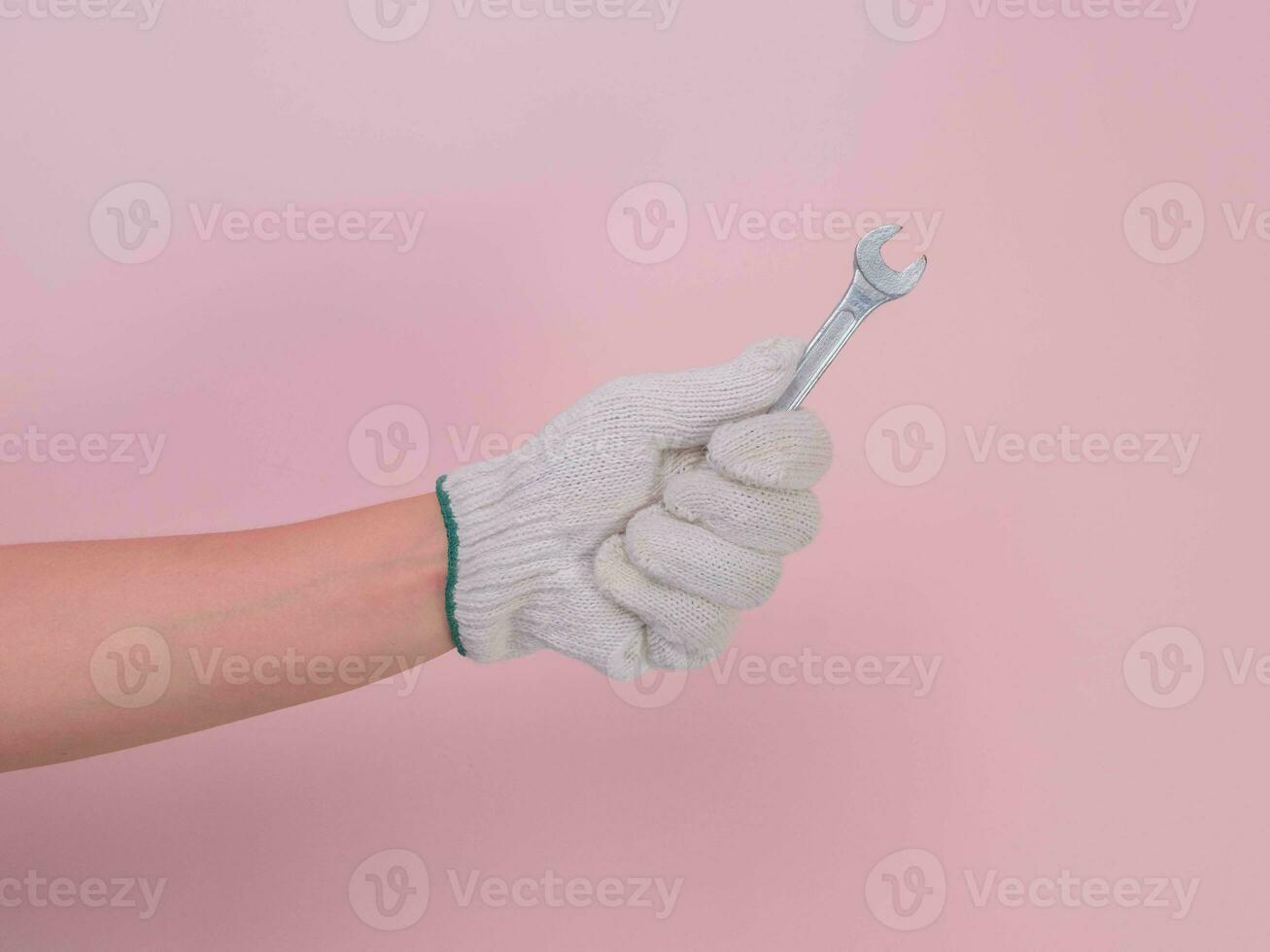 mano nel bianca a maglia guanto Tenere metallo chiave inglese isolato su rosa sfondo. lavoratori mano nel un' guanto Tenere un' chiave inglese. foto