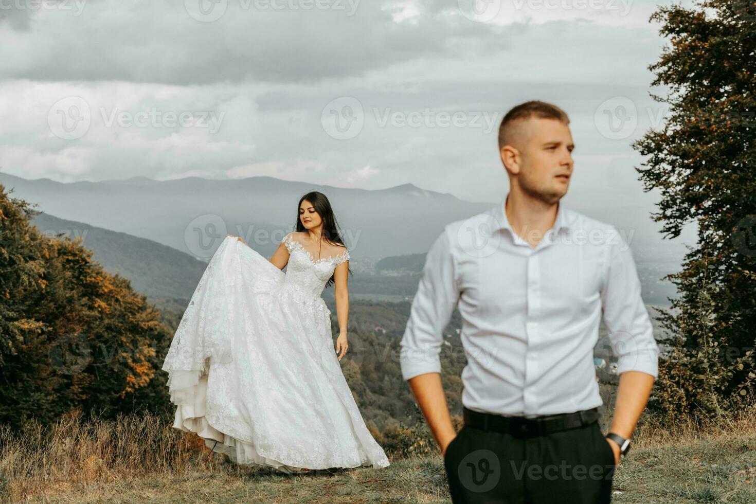 bellissimo sposa e sposo su il sfondo di autunno montagne nel davanti. un' lussuoso bianca vestito svolazza. il sposa è nel il sfondo. nozze cerimonia su superiore di il montagna. gratuito spazio. foto