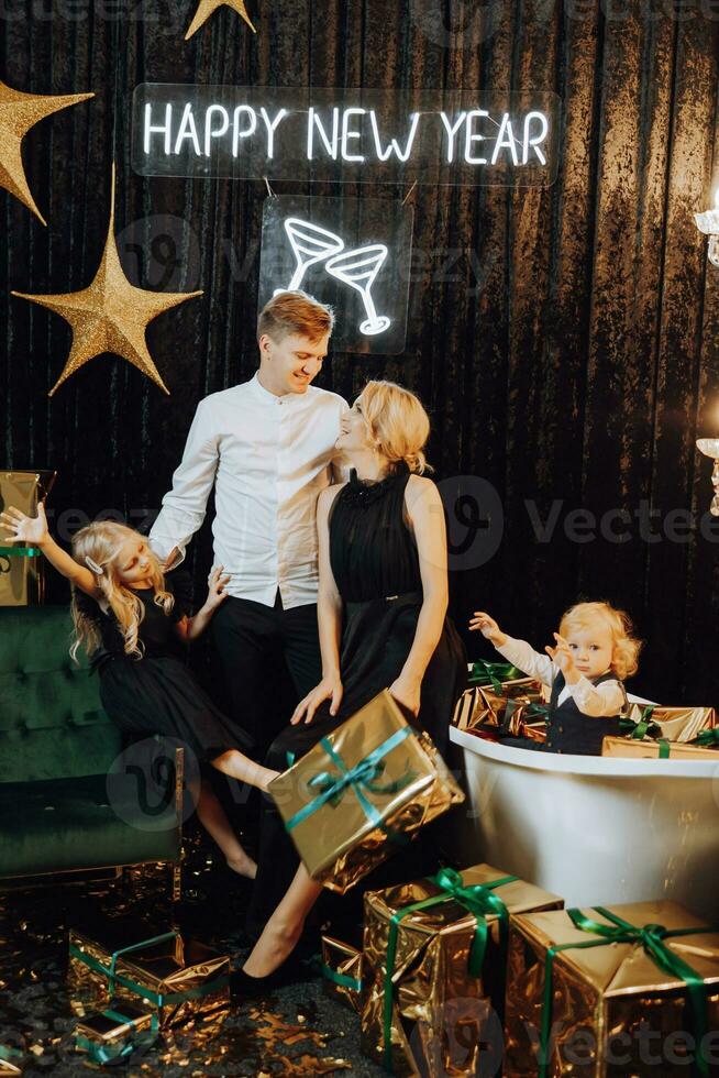 allegro Natale e contento vacanze. allegro e contento famiglia con Natale regali nel d'oro involucri e buio sfondo. bambini siamo avendo divertimento. amorevole famiglia con i regali nel il camera. foto