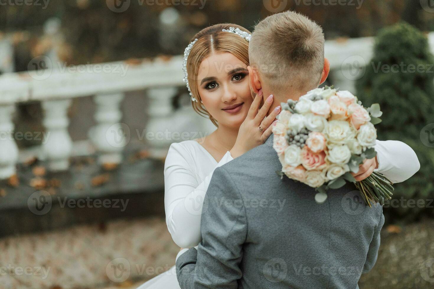il sposo abbracci il sposa e baci suo, il sposa sembra a il telecamera. nozze camminare nel il giardino foto
