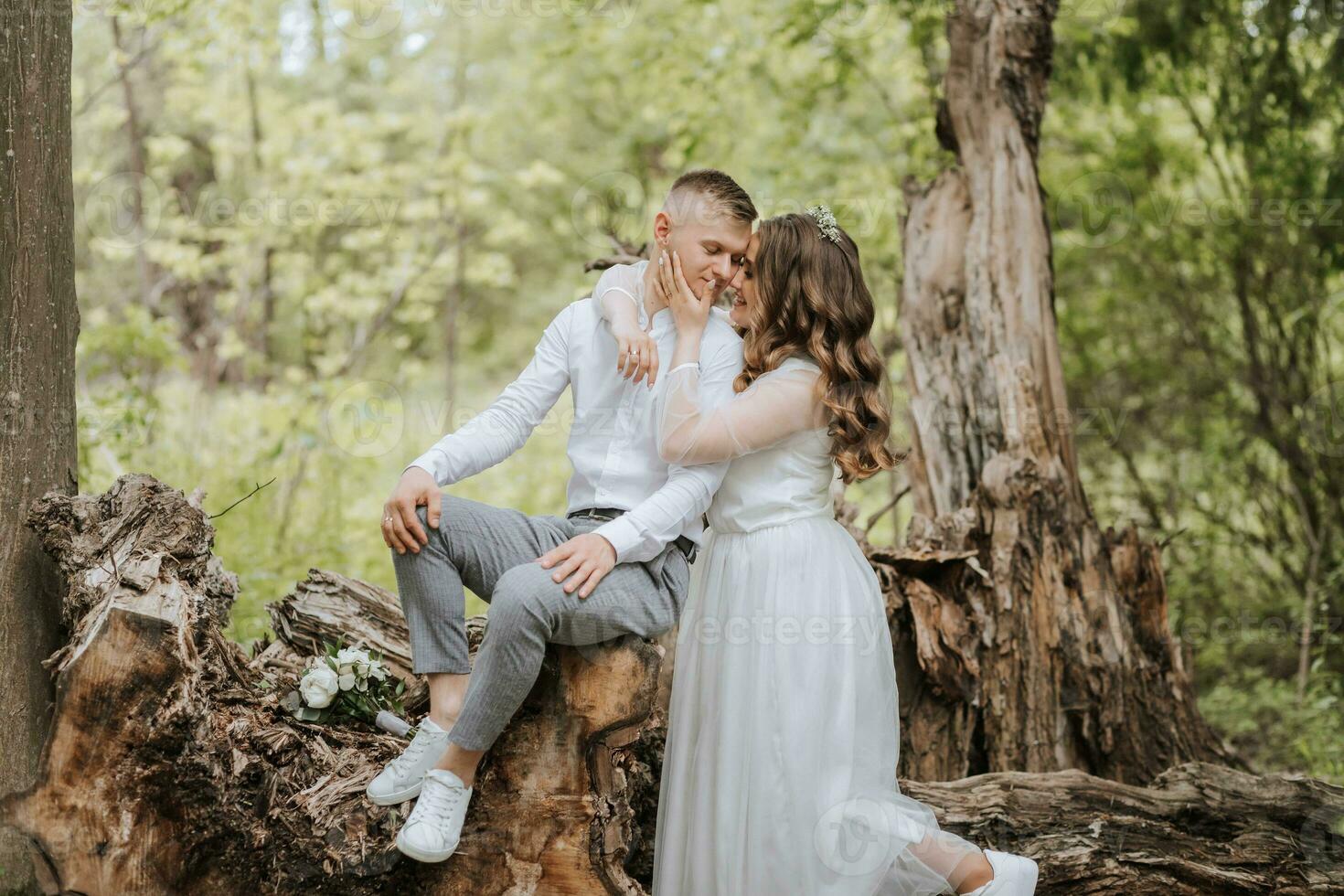 dolce abbraccio di il sposa e sposo nel il foresta. il sposo è vestito nel un' bianca camicia e grigio pantaloni, il sposa è nel un' leggero bianca vestito foto