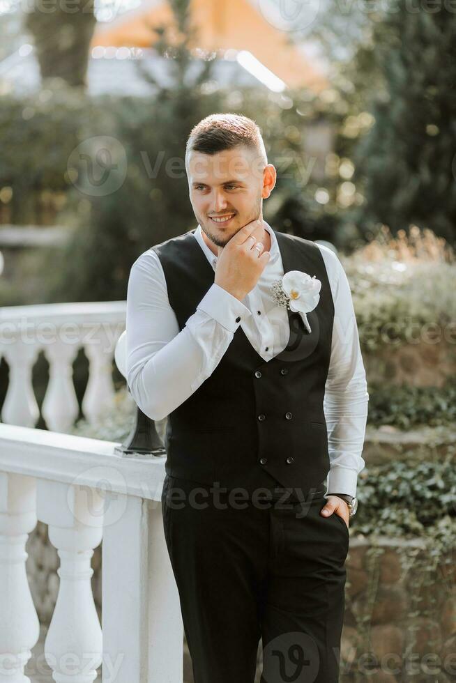 Candido ritratto di giovane elegante sposo nel classico nero completo da uomo con panciotto, bianca camicia foto