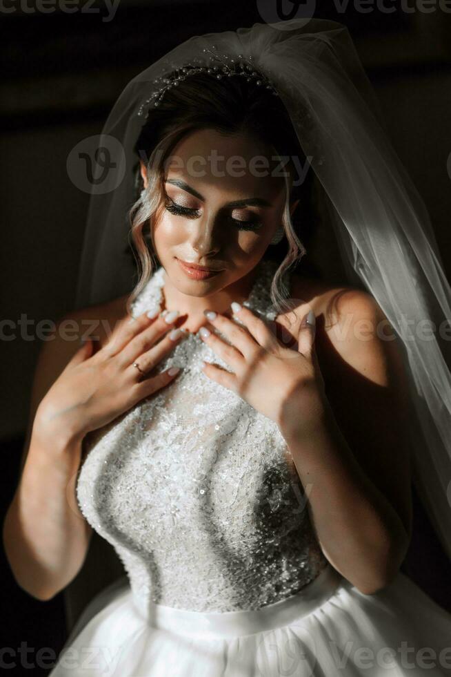 contento e bellissimo sposa con velo avvicinamento. sposa con professionale trucco e acconciatura su un' buio sfondo. foto