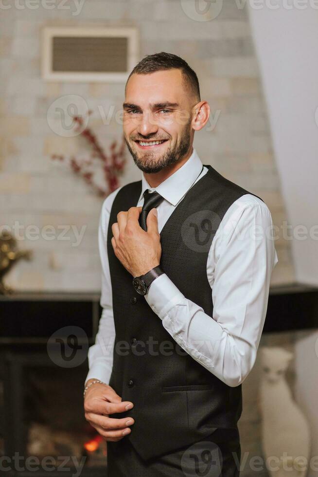 ritratto di un' uomo nel un' bianca camicia, panciotto e nero cravatta nel un' camera con naturale luce. il sposo è preparazione per il nozze. il uomo è indossare un' bianca camicia. elegante sposo foto