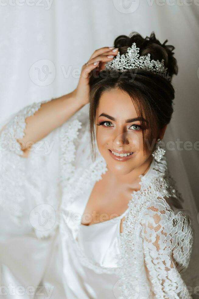 bellissima sposa ritratto nel sua accappatoio indossare tiara. bellissimo bridal trucco e acconciatura e capelli Accessori. sposa per essere sorridente ritratto foto