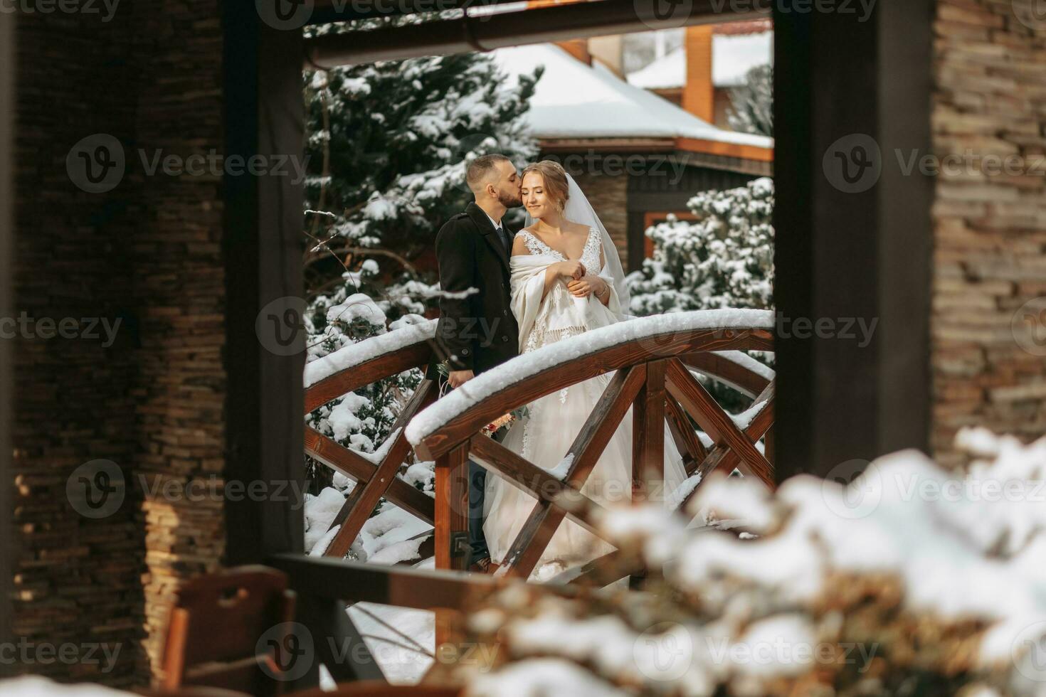 contento sposa e sposo abbraccio tra nevoso alberi. sposo e sposa nel il inverno parco. sposa con un' mazzo di fiori nel un' nozze vestito e poncho. sposo nel un' nero cappotto. foto