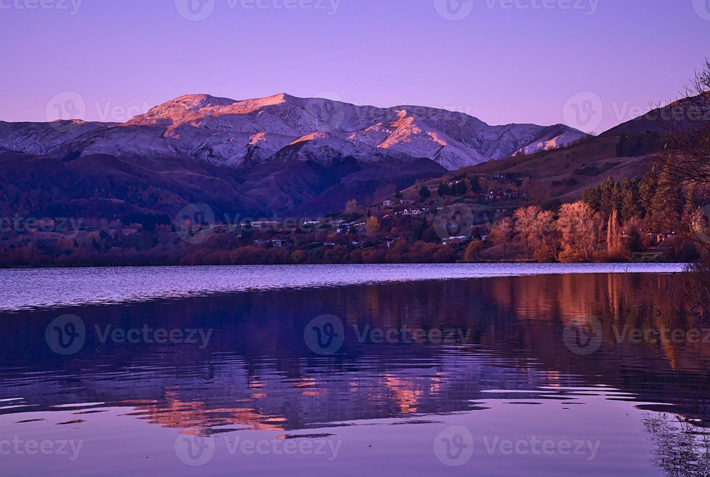 piccolo paese con le montagne di fronte a un lago foto