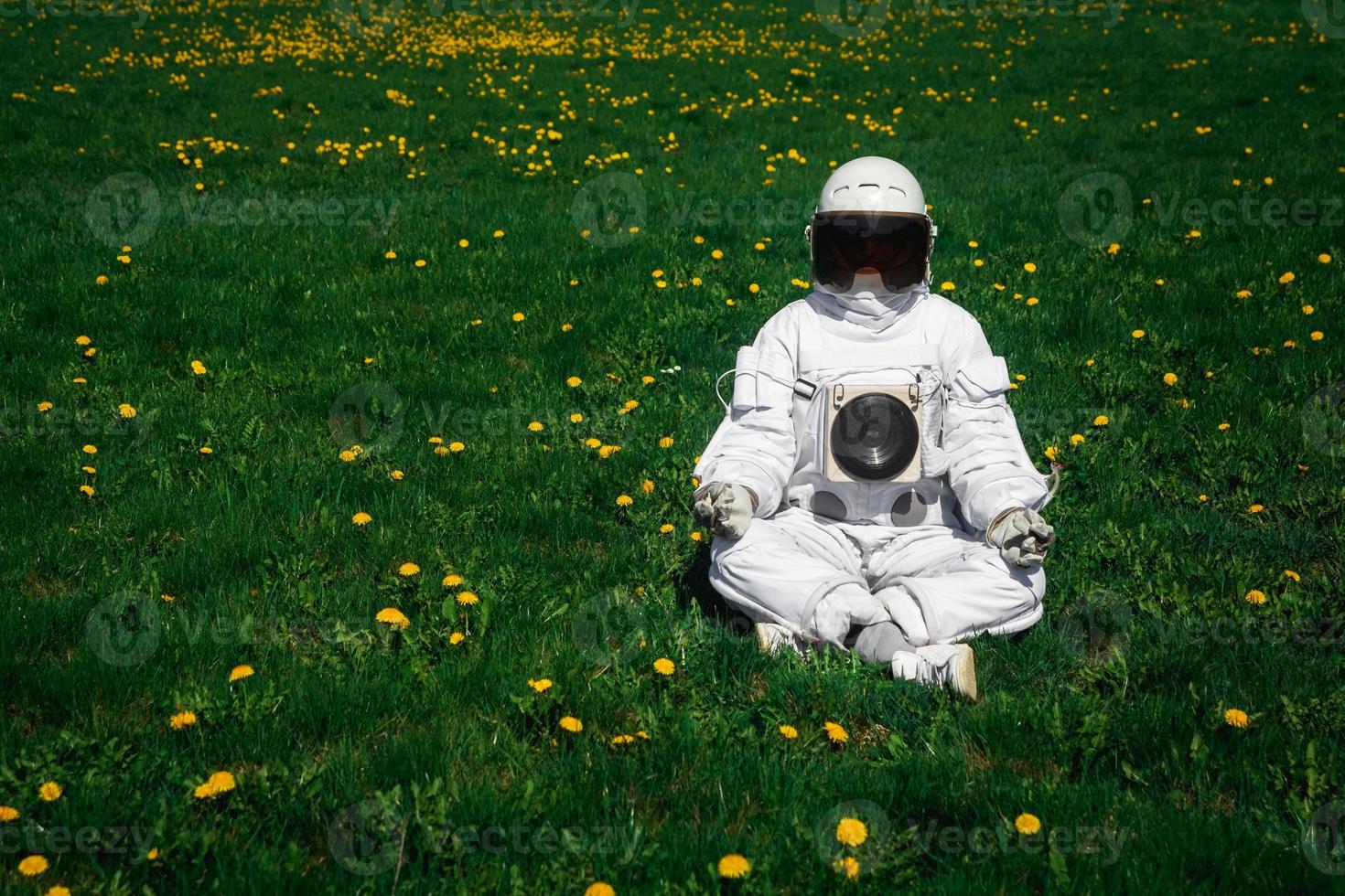 astronauta futuristico in un casco si siede su un prato verde una posizione meditativa foto