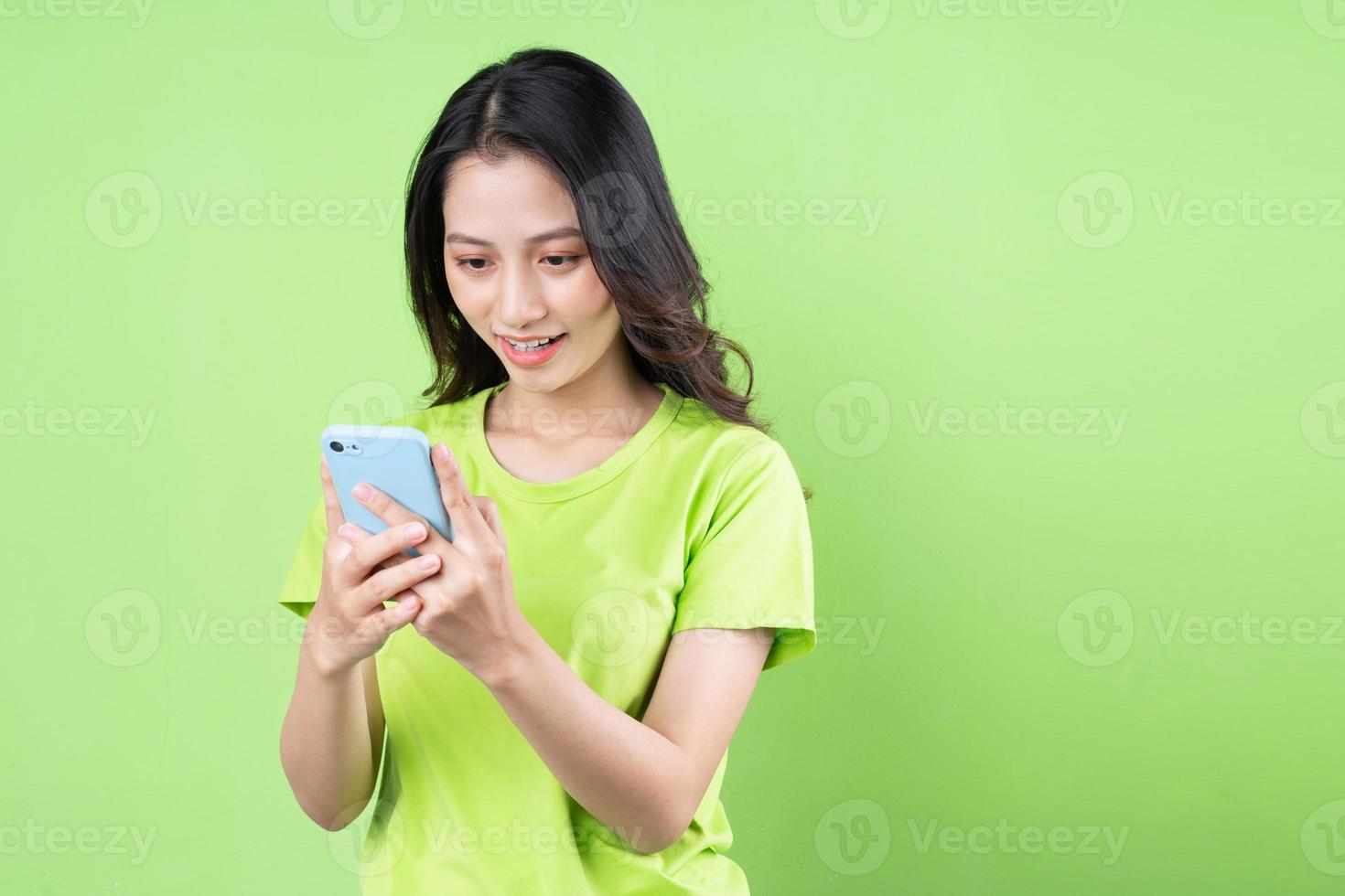 immagine di una giovane donna asiatica che tiene in mano uno smartphone su sfondo verde foto