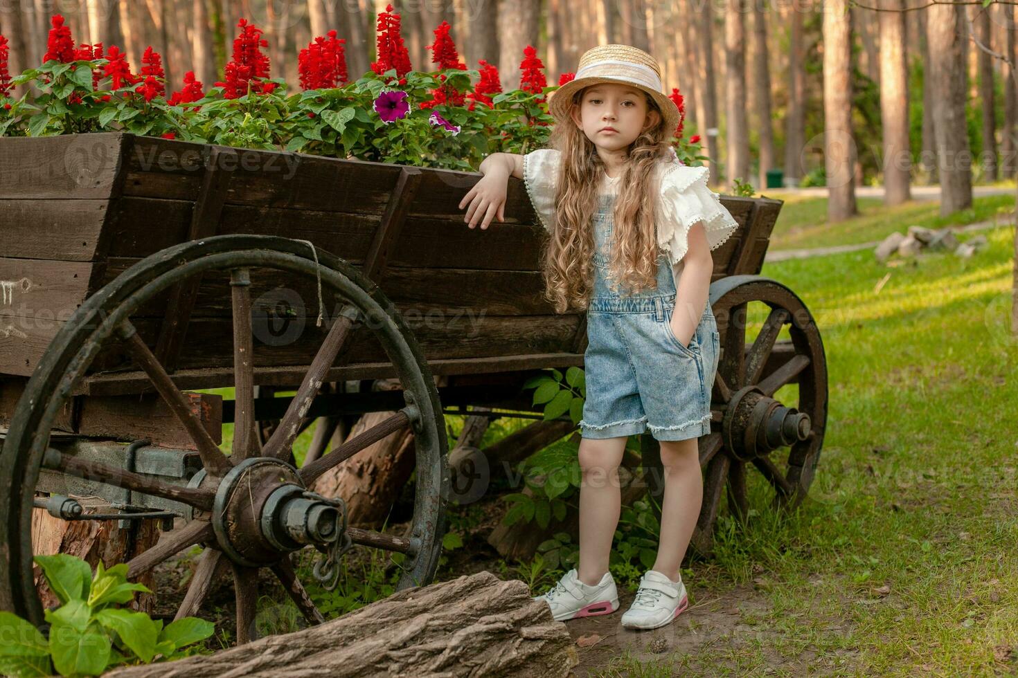 poco ragazza pendente Vintage ▾ di legno carrello Usato come letto di fiori nel estate parco foto