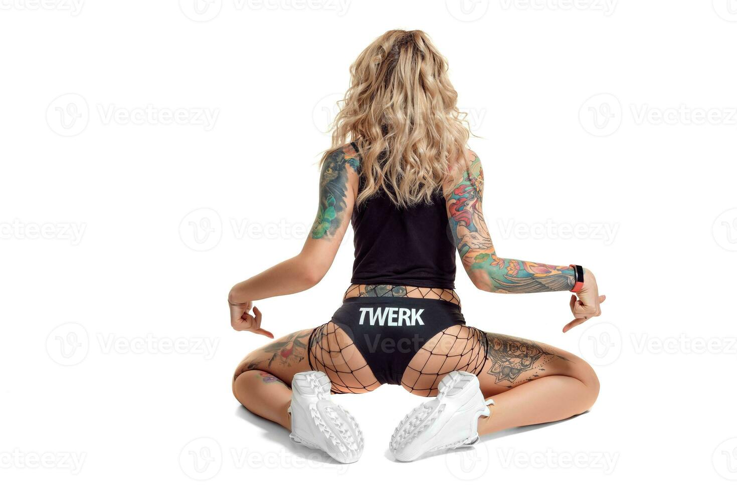 sexy biondo twerk donna con tatuato corpo e lungo Riccio capelli è in posa nel studio. foto