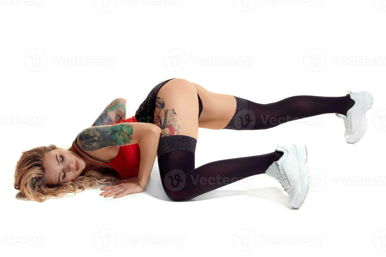 sexy biondo twerk donna con tatuato corpo e lungo Riccio capelli è in posa nel studio. foto