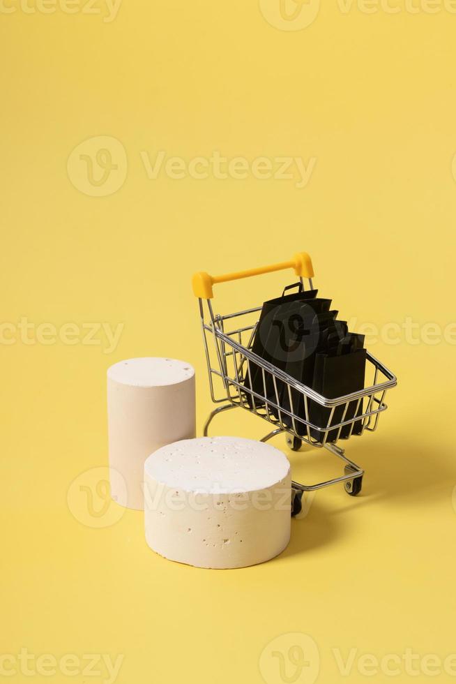 podi o piedistalli finti vuoti e carrello per supermercati in miniatura con borse della spesa in vendita venerdì nero su sfondo giallo foto
