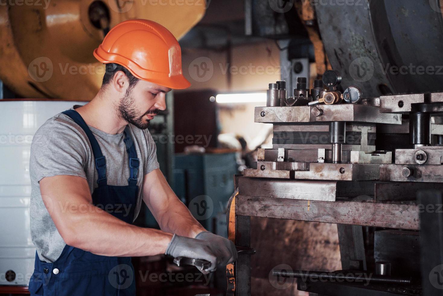ritratto di un giovane lavoratore con un elmetto in un grande impianto di lavorazione dei metalli. l'ingegnere serve le macchine e produce parti per apparecchiature a gas foto