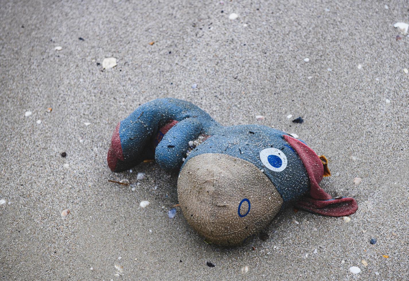 scartare la vecchia bambola di stoffa della spazzatura sulla spiaggia. foto