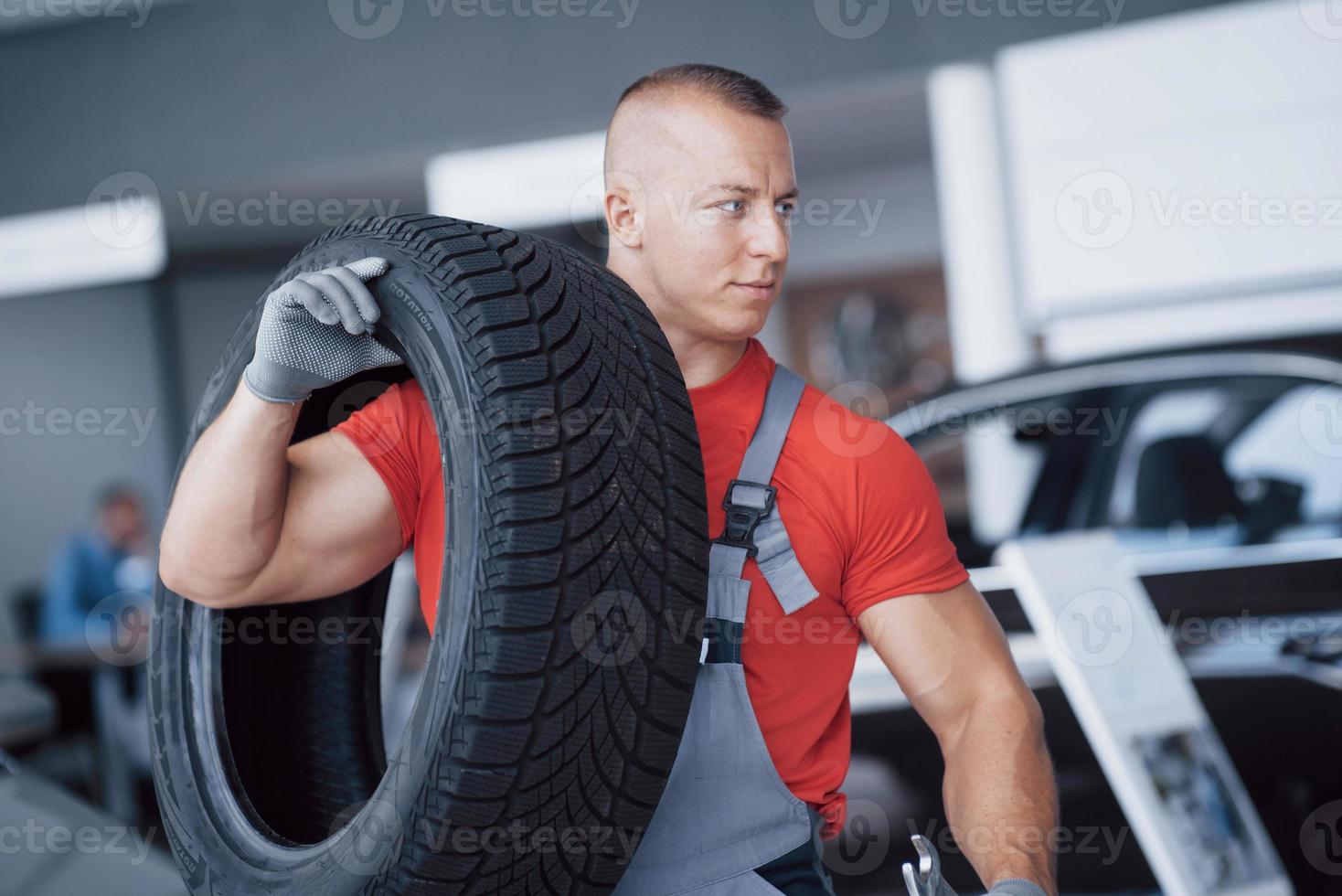 meccanico che tiene un pneumatico al garage di riparazione. sostituzione gomme invernali ed estive foto