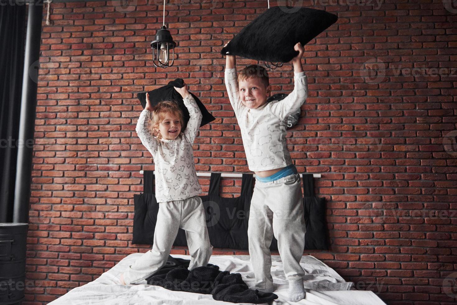 bambini cattivi ragazzino e ragazza hanno messo in scena una battaglia di cuscini sul letto in camera da letto. a loro piace quel tipo di gioco foto