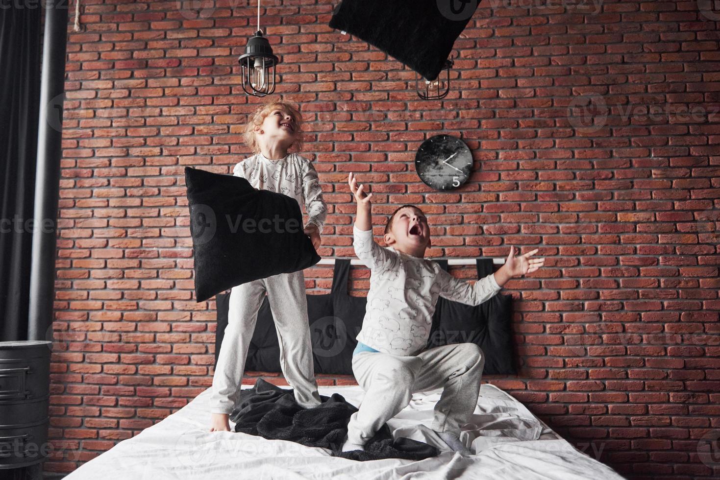 bambini cattivi ragazzino e ragazza hanno messo in scena una battaglia di cuscini sul letto in camera da letto. a loro piace quel tipo di gioco foto