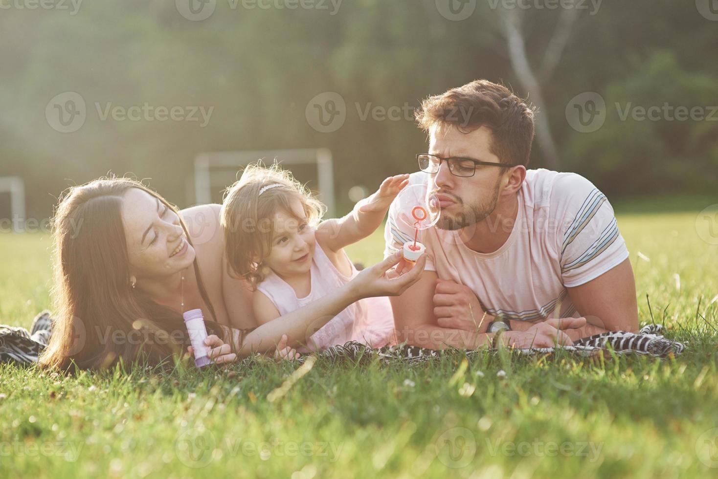 madre e padre trascorrono del tempo insieme felici. la piccola figlia gioca con i suoi genitori all'aperto durante il tramonto foto
